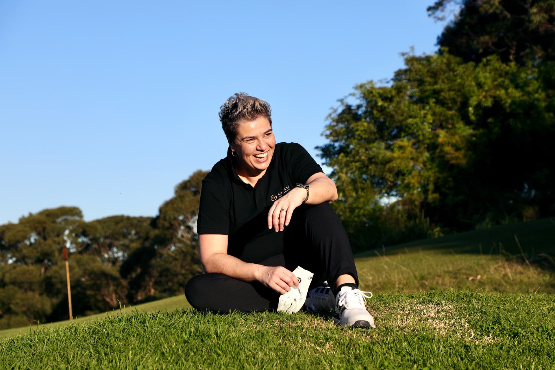 Evonne Englezos, founder of Golf And Talk, smiling while seated on a golf course